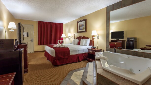 A hotel room with a large bed, a sitting area with a desk and chair, a bathtub, and a television. - Angel Inn Central (Branson)