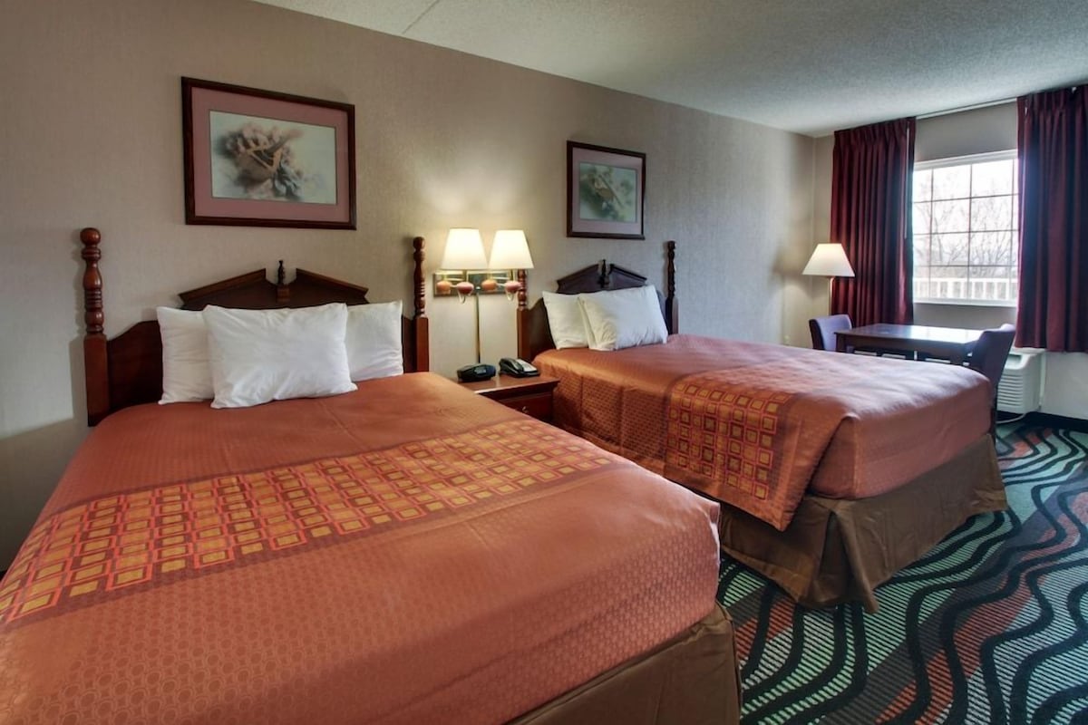 A hotel room with two beds, a desk, a chair, and a window with curtains.