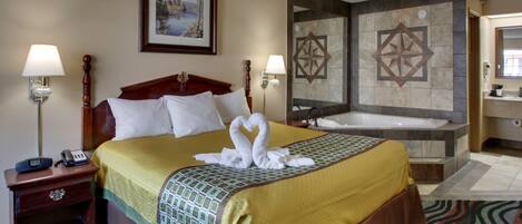 A hotel room with a large bed, two bedside lamps, a framed picture on the wall, a bathtub, and a bathroom with a large mirror.