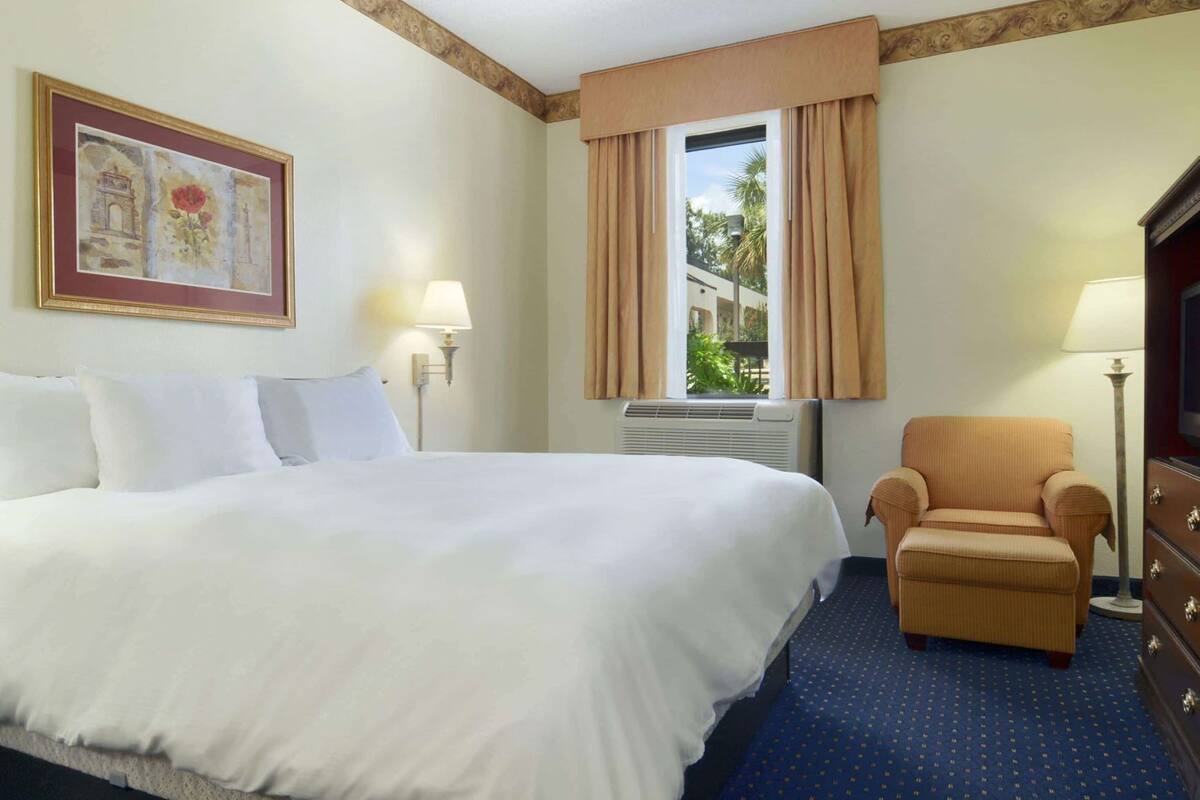 Een hotelkamer met een groot bed, een stoel, een televisie en een raam met gordijnen.
