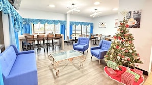 A spacious room with blue upholstered chairs, a glass coffee table, and a decorated Christmas tree.