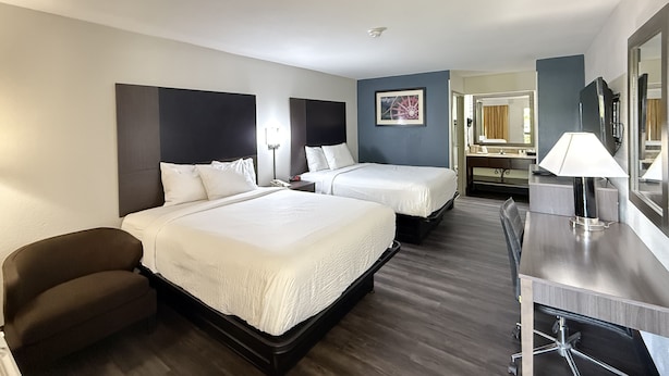 A hotel room with two beds, a desk, a chair, a mirror, and a picture on the wall.