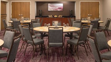A conference room with a round table, grey upholstered chairs, a coffee station, and a large abstract painting on the wall.