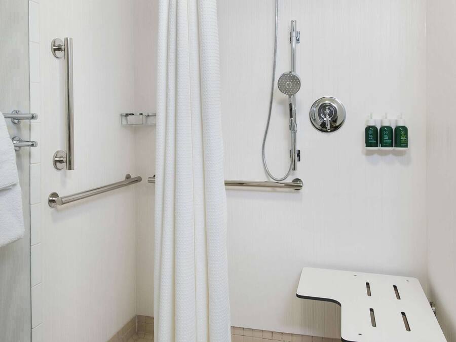 A shower area with a white curtain, grab bars, a handheld showerhead, and a small table.