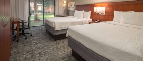 A hotel room with two beds, a desk, and a view of the outdoors.