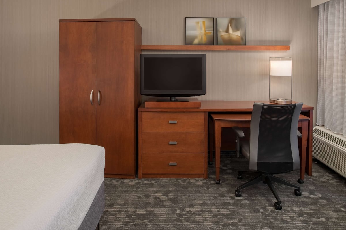 Une chambre d’hôtel équipée d’un lit, d’un bureau avec un ordinateur, d’une chaise, d’une télévision et d’une lampe.