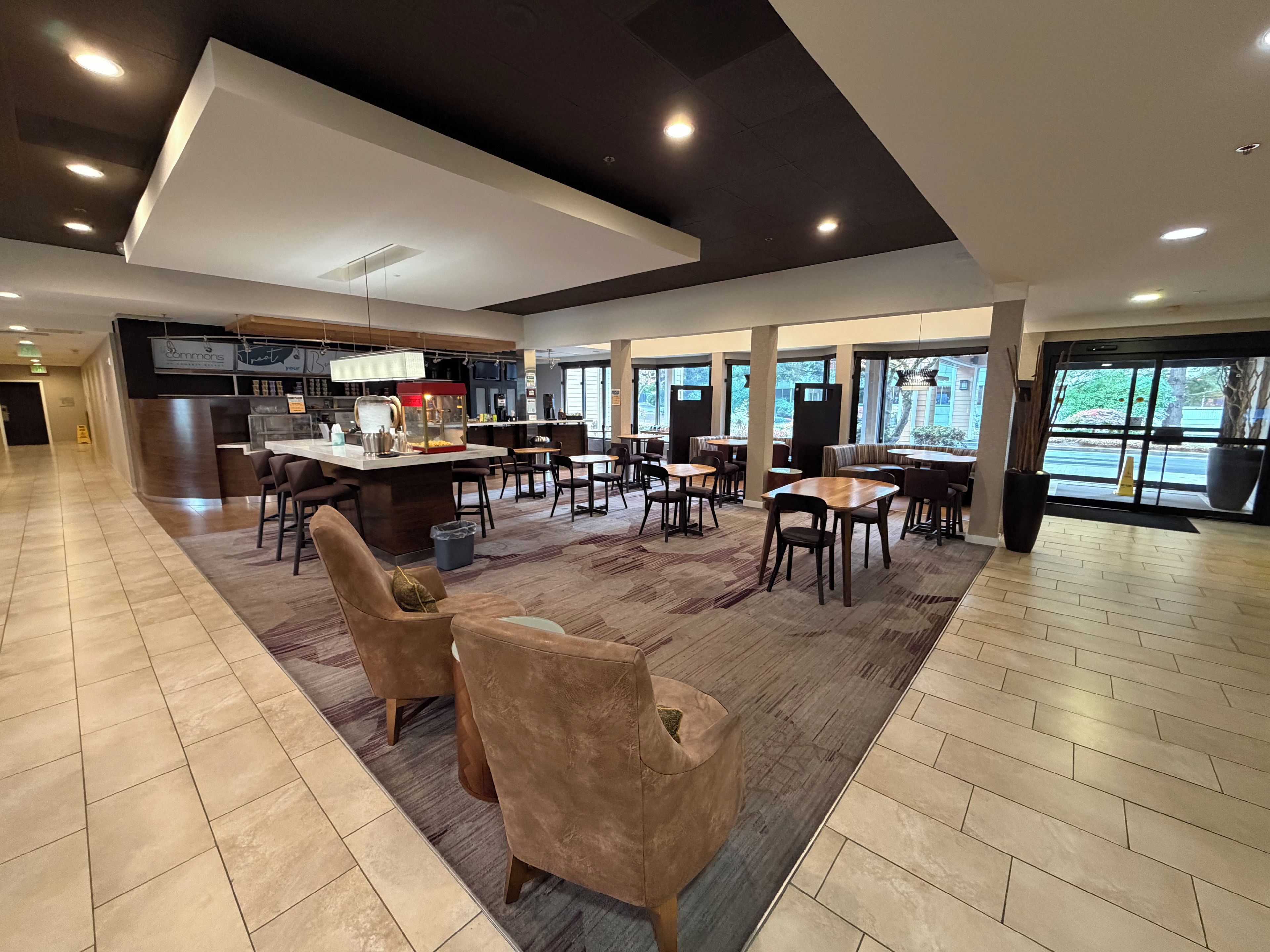 A spacious hotel lobby with a central bar area, seating arrangements, and large windows providing natural light.