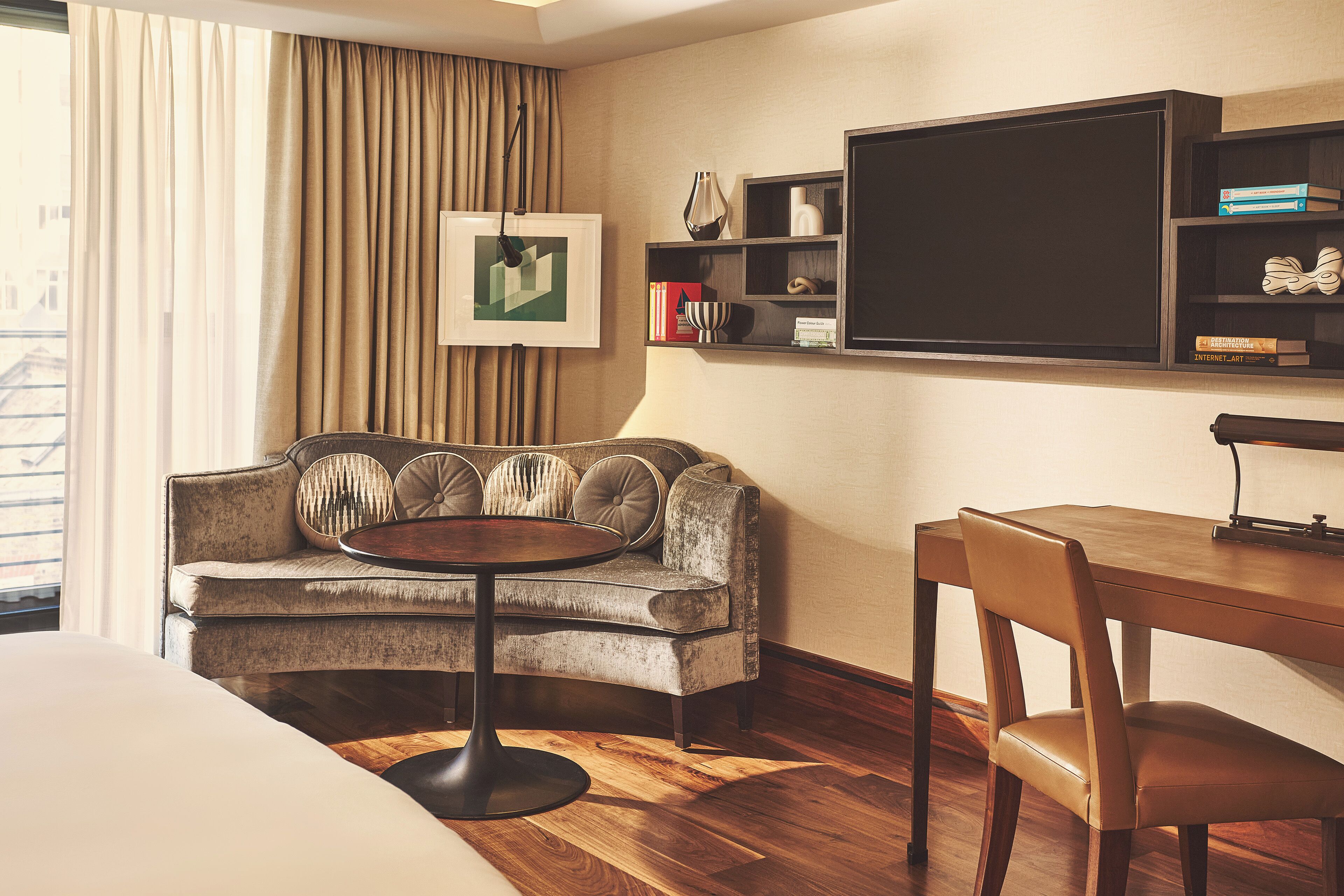 Habitación de hotel con sofá, mesa de comedor, televisión y estantería.