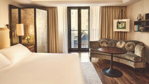 A hotel room with a large bed, a sofa, a small table, a bookshelf, and a view through a sliding door.