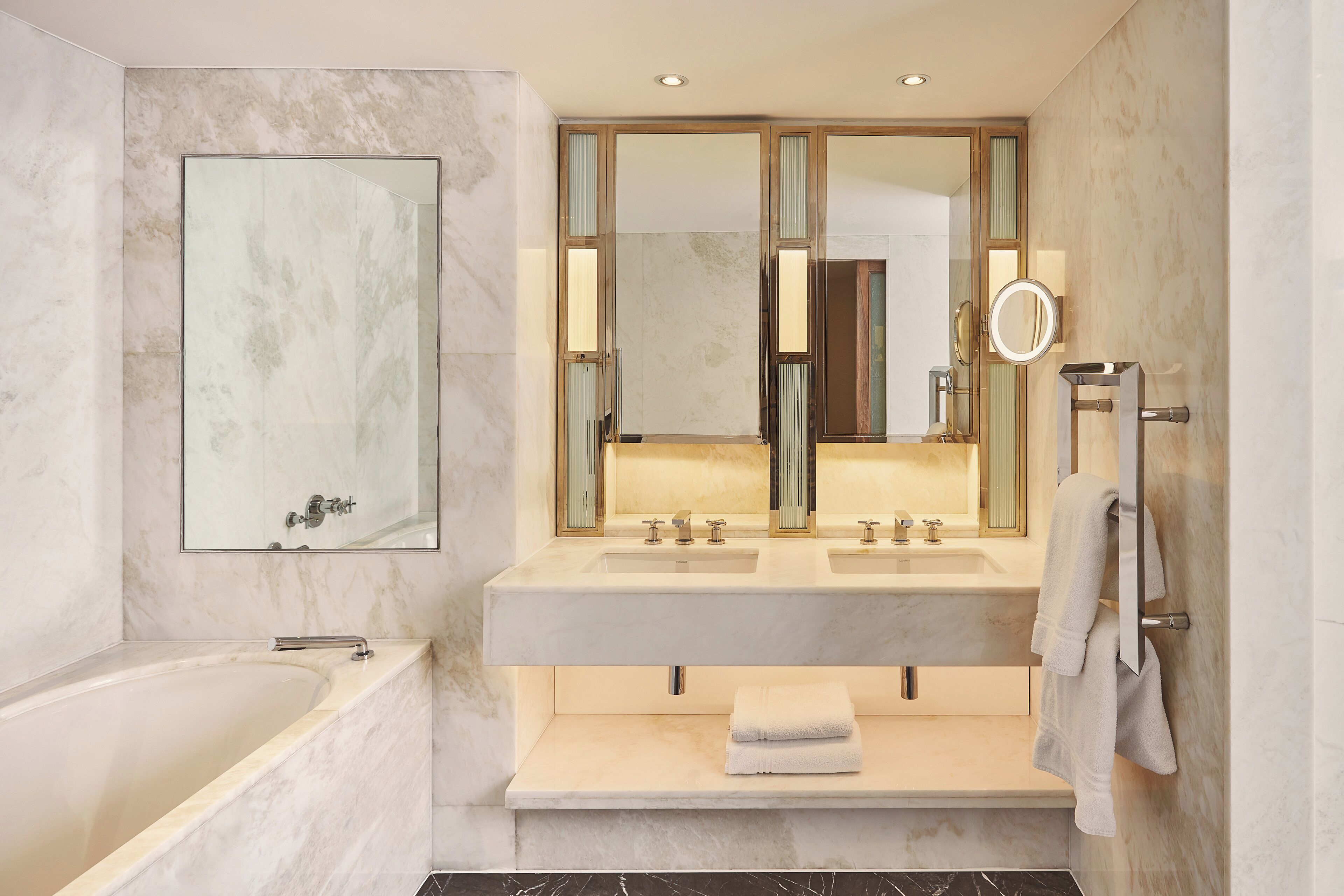 A modern bathroom with a bathtub, two sinks, a vanity, and a large mirror.