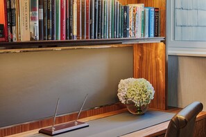 A bookshelf filled with books, a wooden desk with a pen holder, and a vase with flowers.