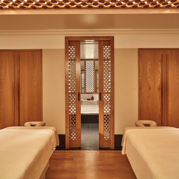 A room with two beds, wooden wardrobes, a decorative wooden screen, and a ceiling with a patterned design.