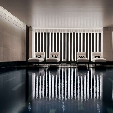 A modern indoor pool area with a sleek design, featuring a reflective floor and a row of white chairs along the wall.