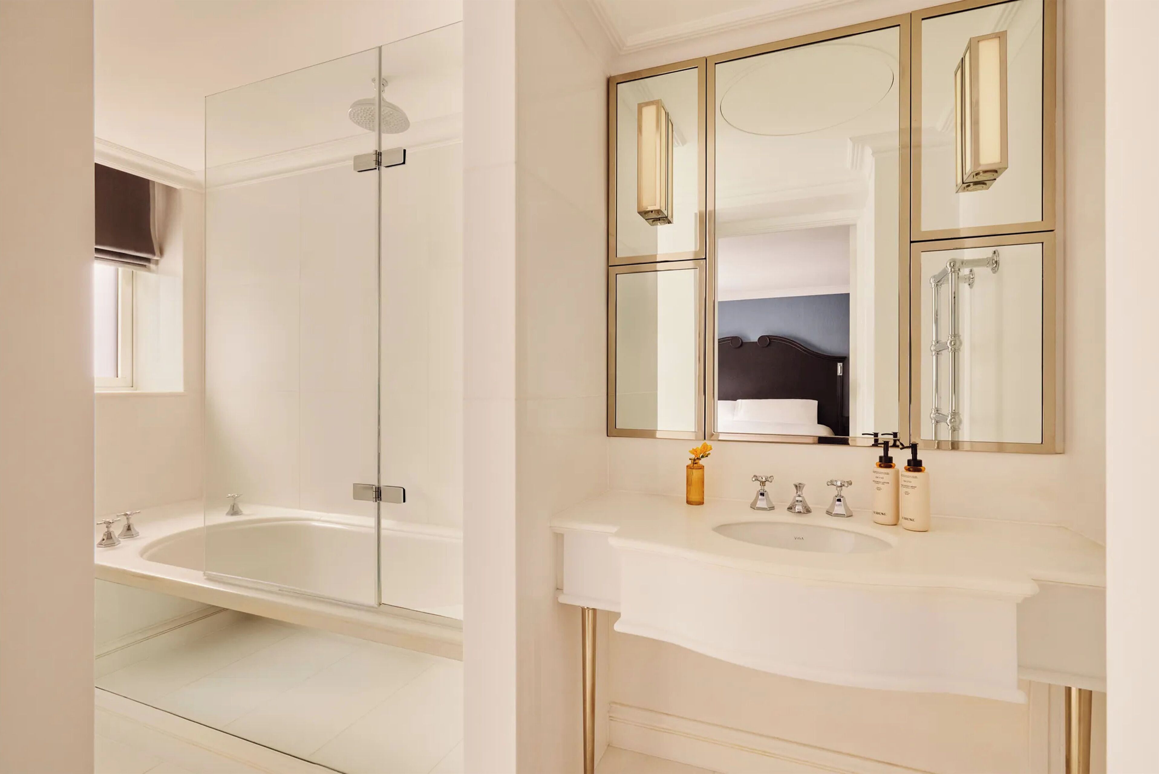 A modern bathroom with a glass-enclosed shower, a white sink with gold fixtures, and a large mirror with gold trim.