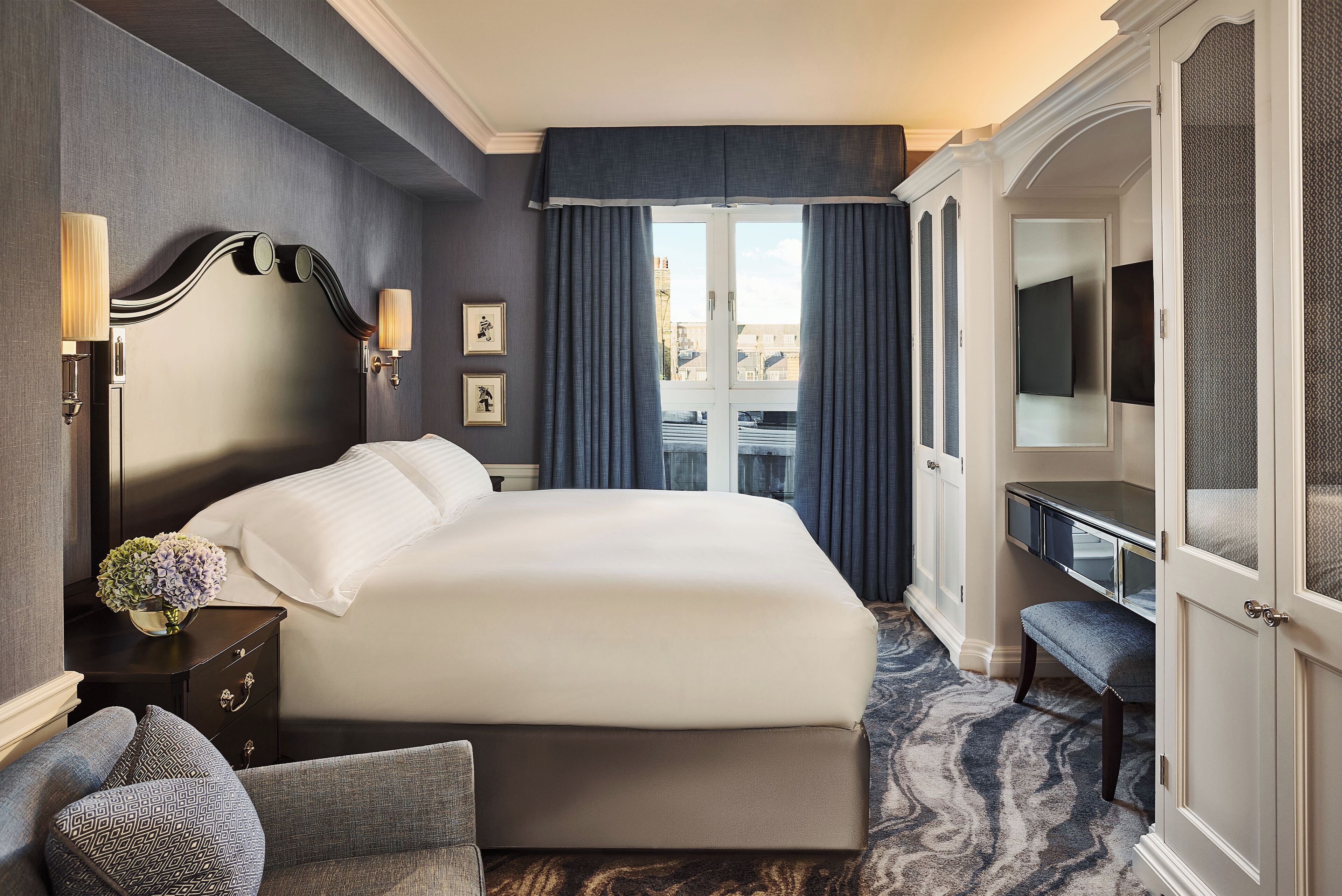 Une chambre d’hôtel avec un grand lit, un bureau, une chaise et une vue sur la ville par la fenêtre.