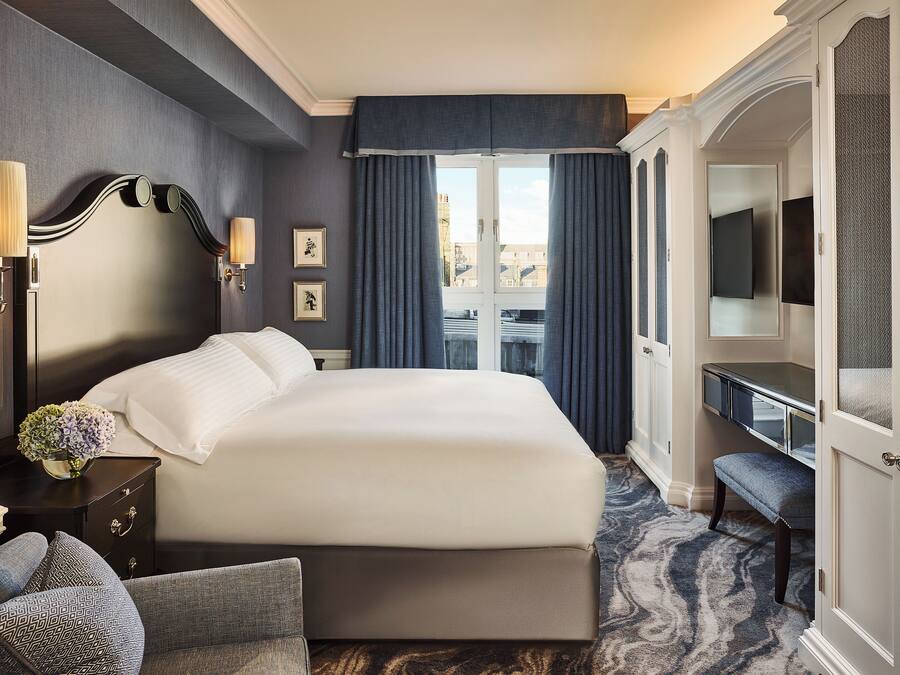 Une chambre d’hôtel avec un grand lit, un bureau, une chaise et une vue sur la ville par la fenêtre.