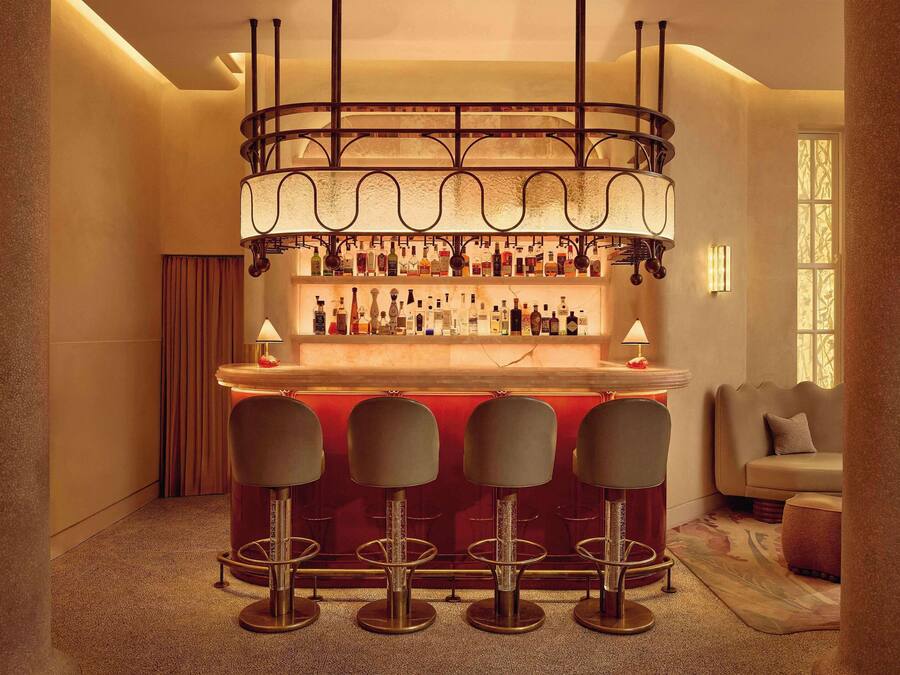 A bar area with a red bar counter, four stools, and a variety of bottles.