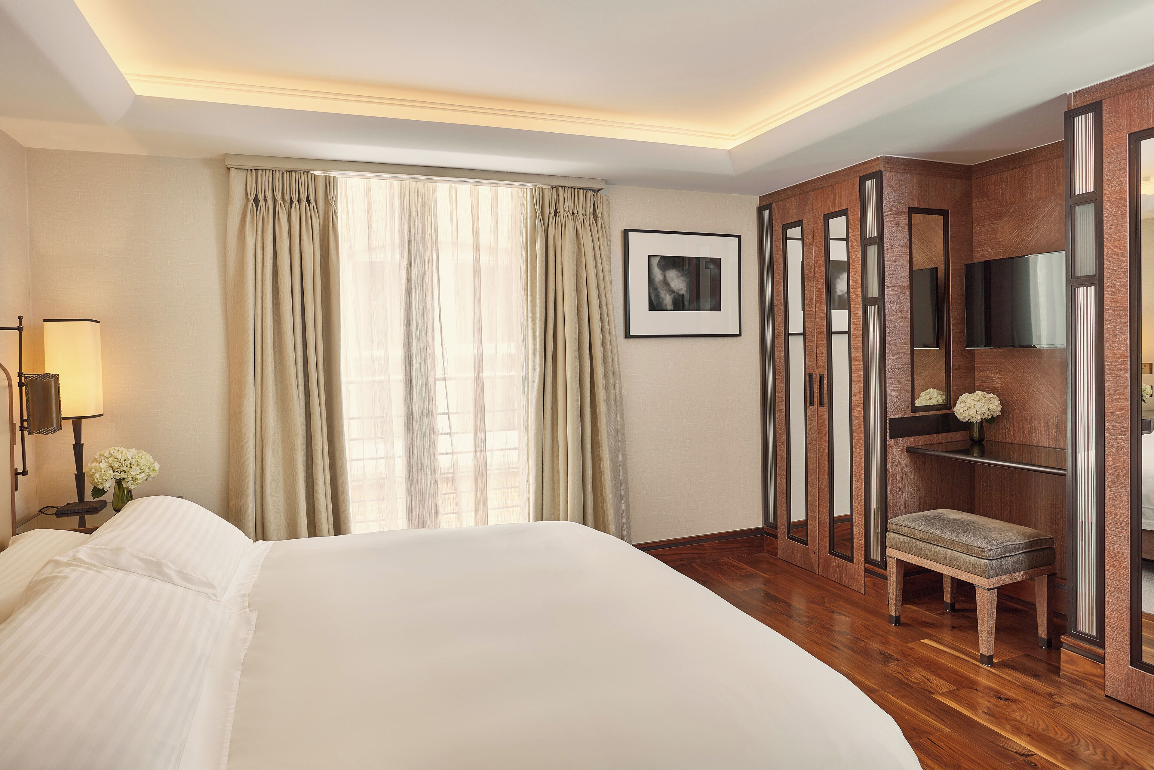 A hotel room with a large bed, a desk with a lamp, a TV, and a wardrobe.