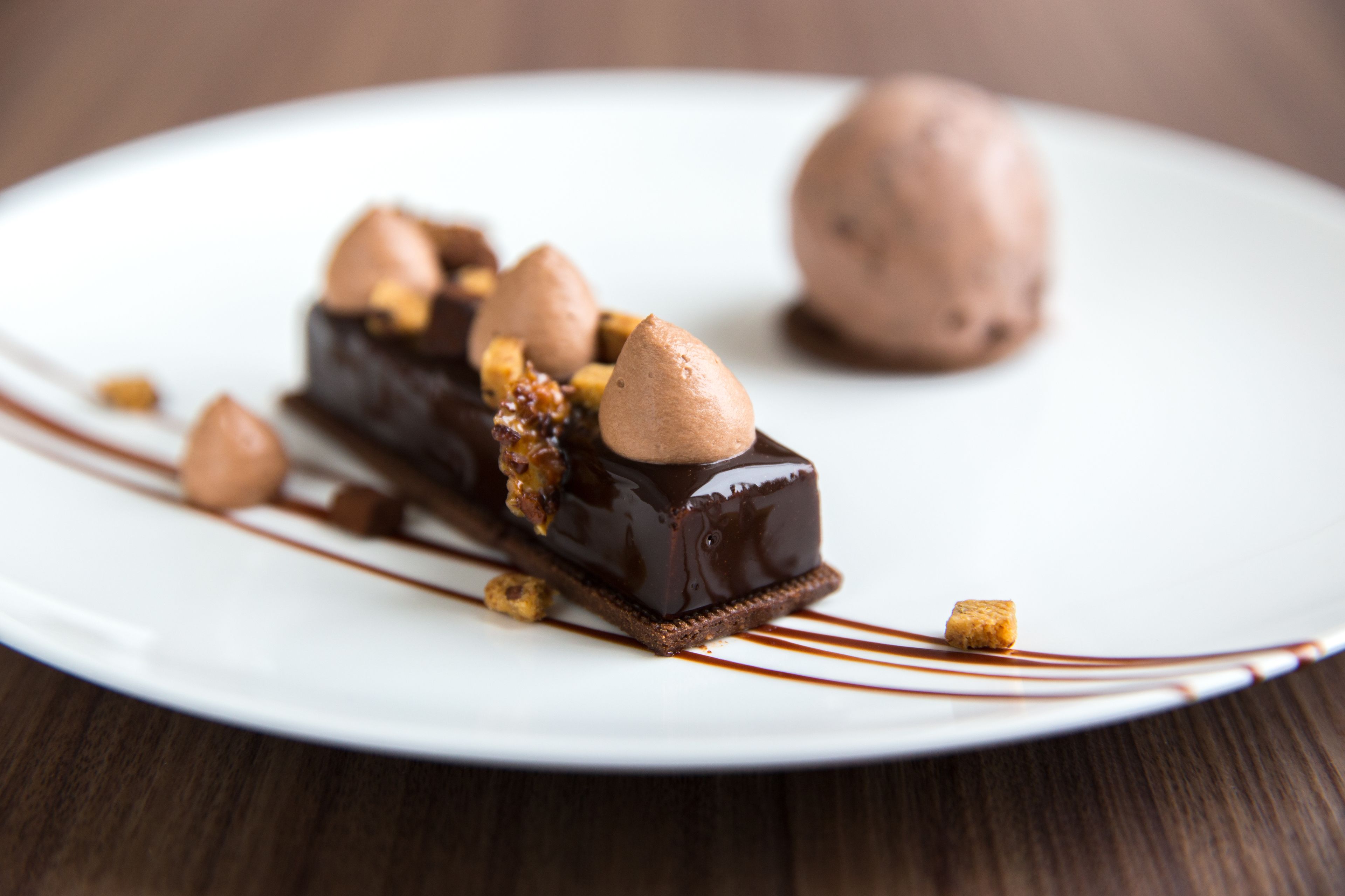 A dessert on a white plate with chocolate sauce and nuts.