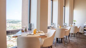 A dining area with high ceilings, large windows, and a city view.