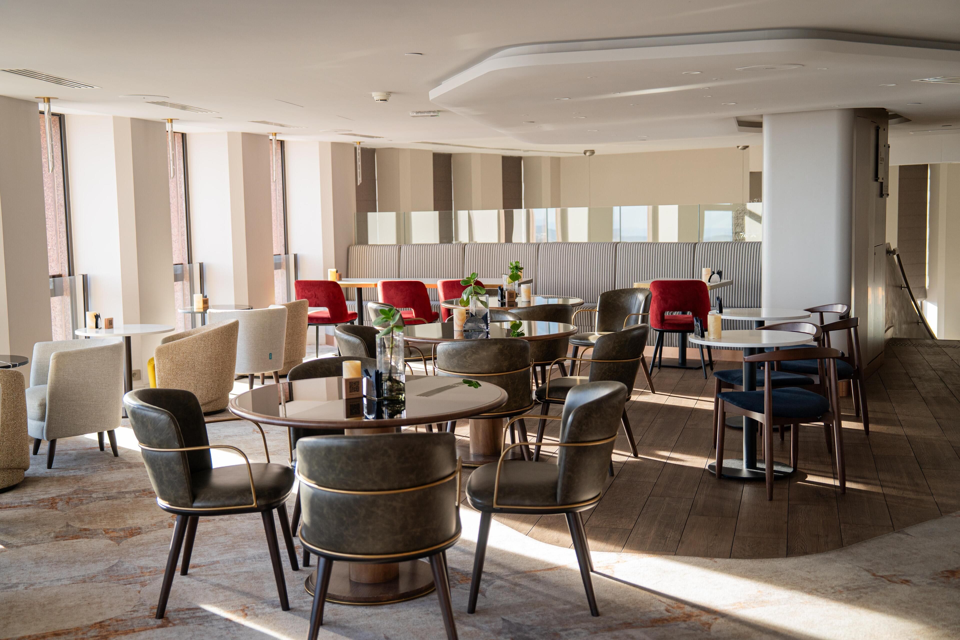 A modern dining area with round tables and chairs, large windows, and a view of the city.