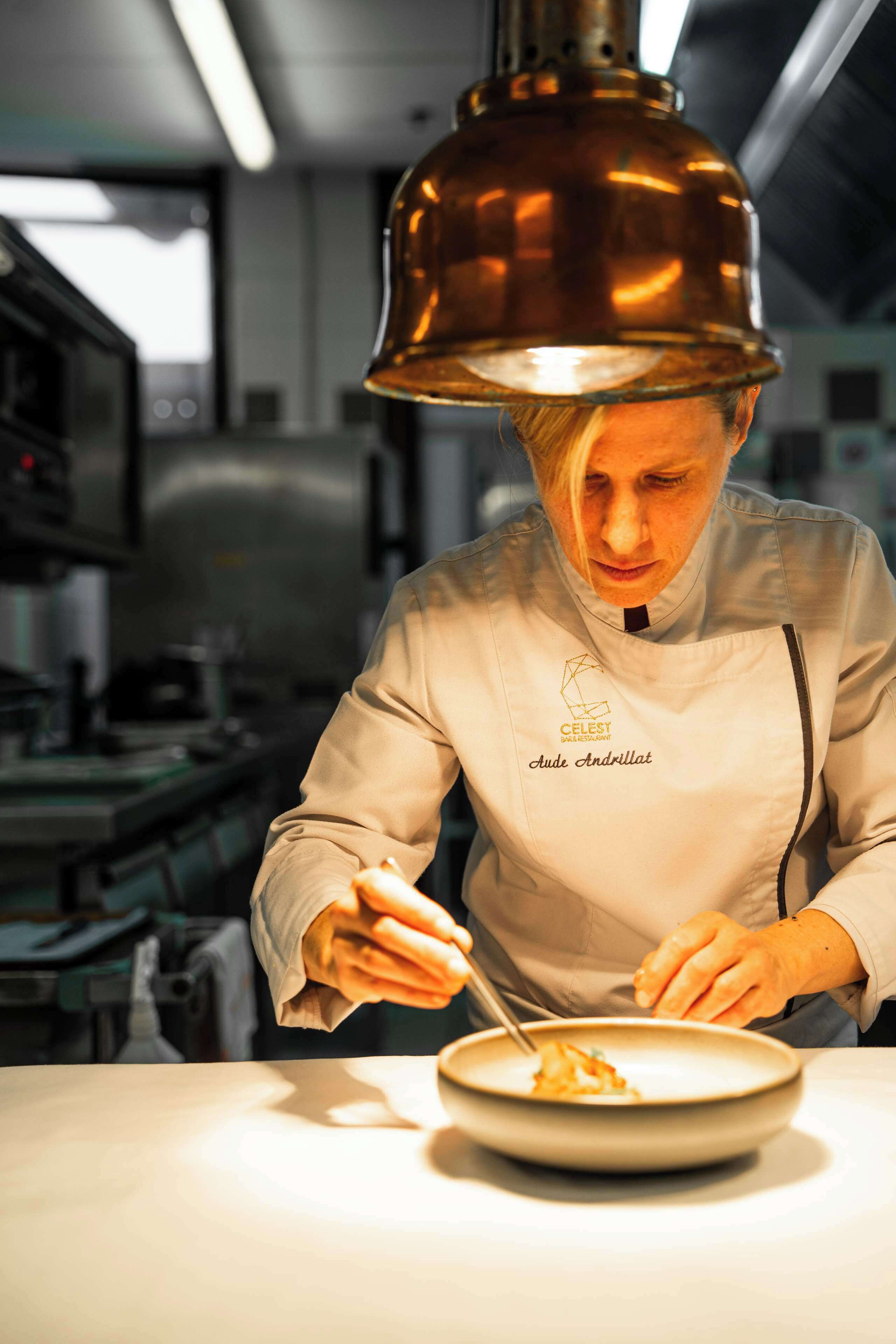 A chef in a professional kitchen, wearing a chef's coat with a name tag.