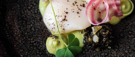 Un plato con textura negra, un elemento blanco, hojas verdes y un toque rosa.