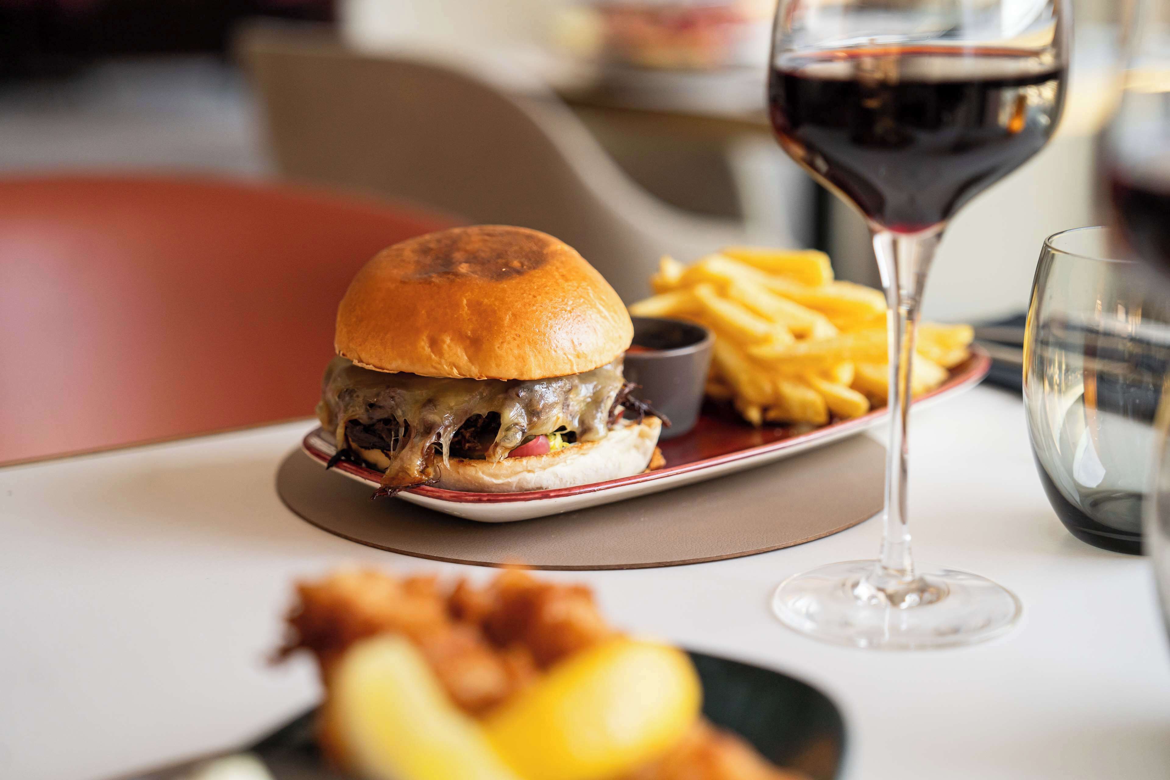 A meal consisting of a burger, fries, and a glass of red wine on a table.
