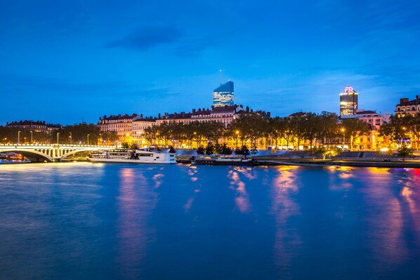 A cityscape at dusk with illuminated buildings, a bridge, and a river reflecting the lights. - Radisson Blu Hotel Lyon (Lyon)