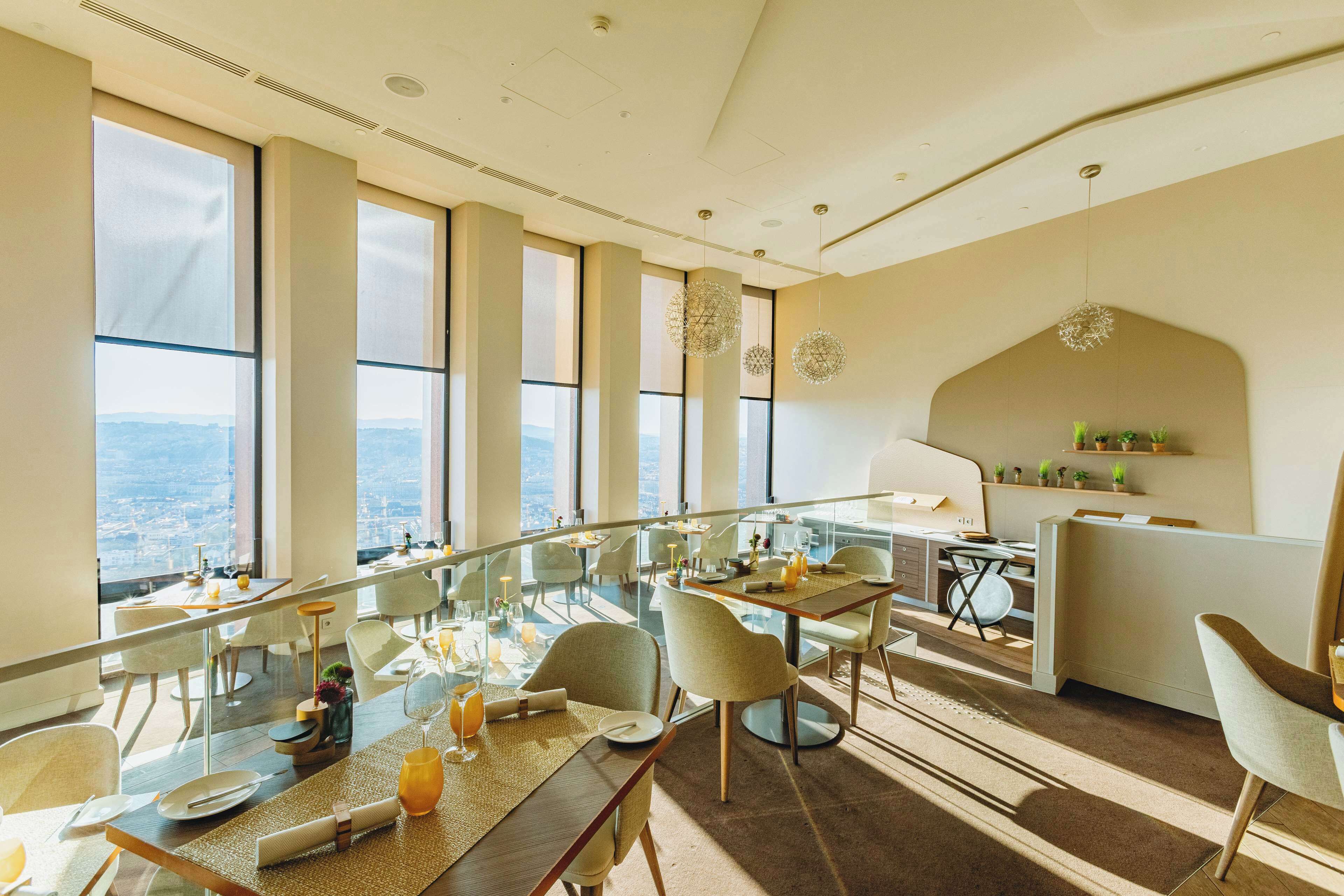 A modern dining area with large windows, a glass partition, and a view of the city.