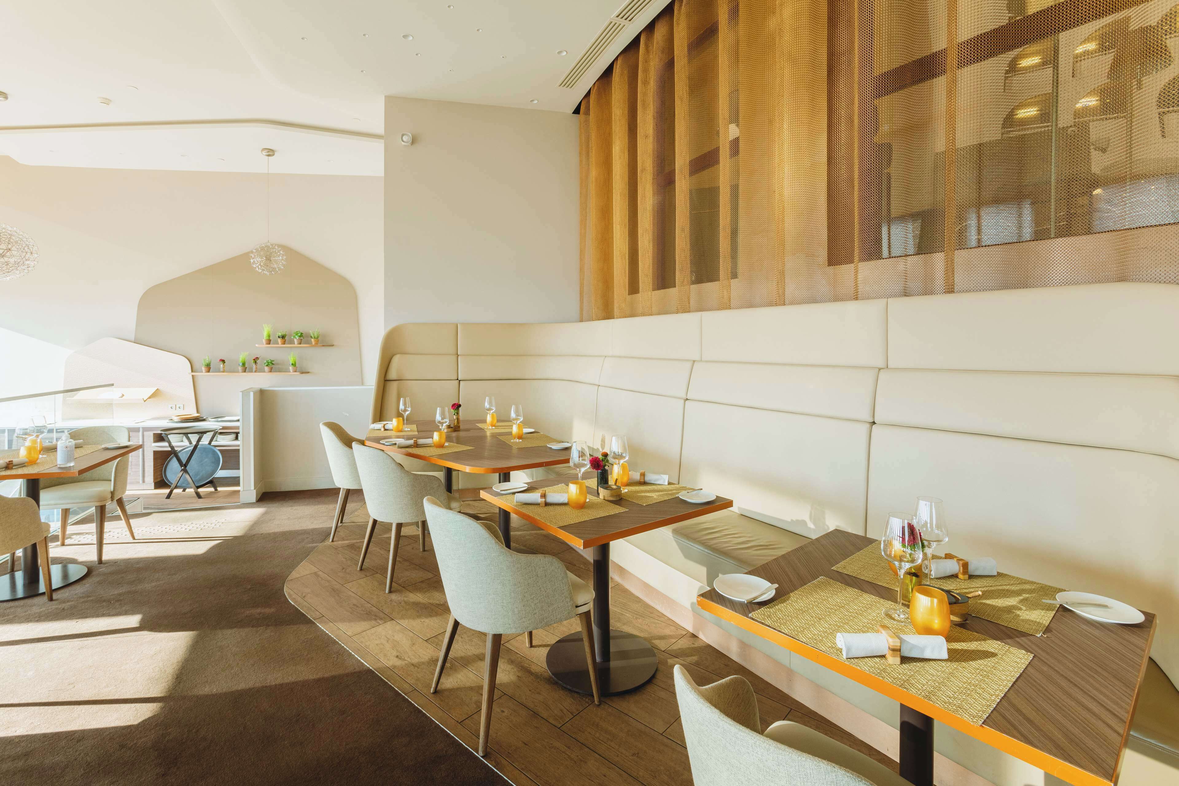 A modern dining area with multiple tables, chairs, and a high ceiling with recessed lighting.
