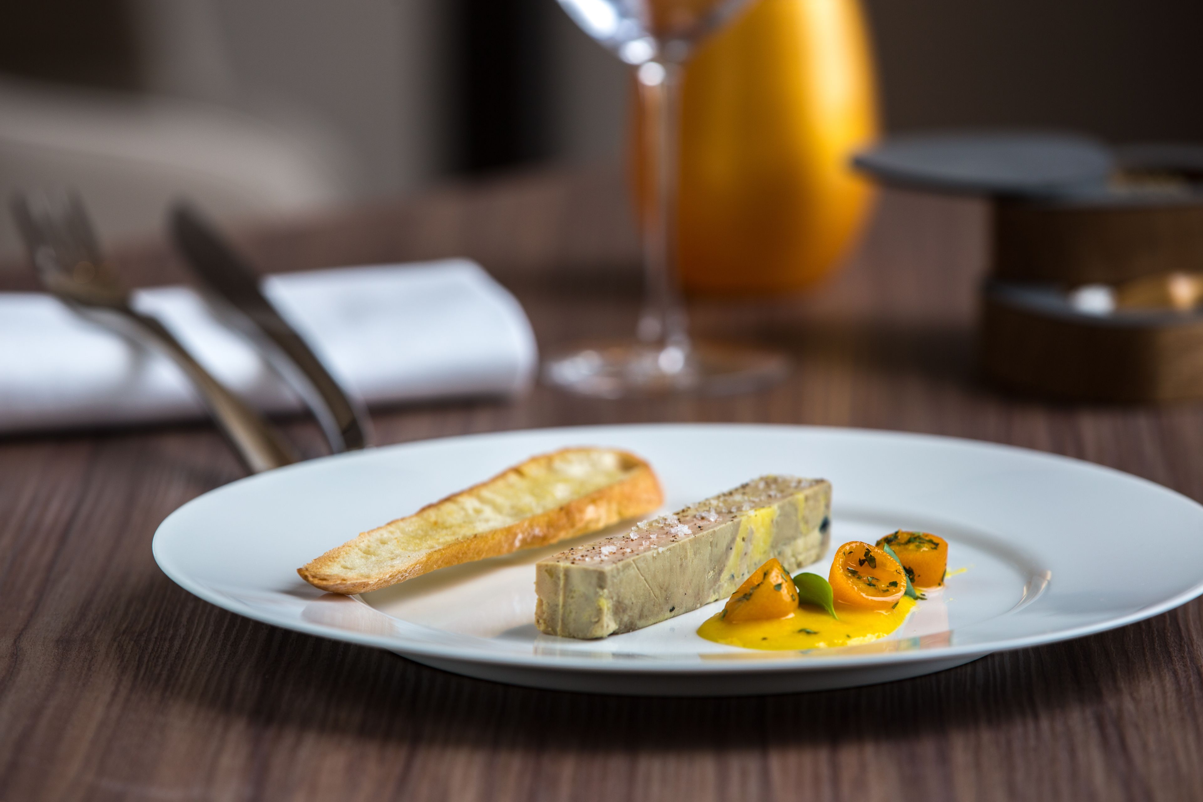 A plate with a slice of bread, a piece of meat, and a small orange garnish on a white plate.