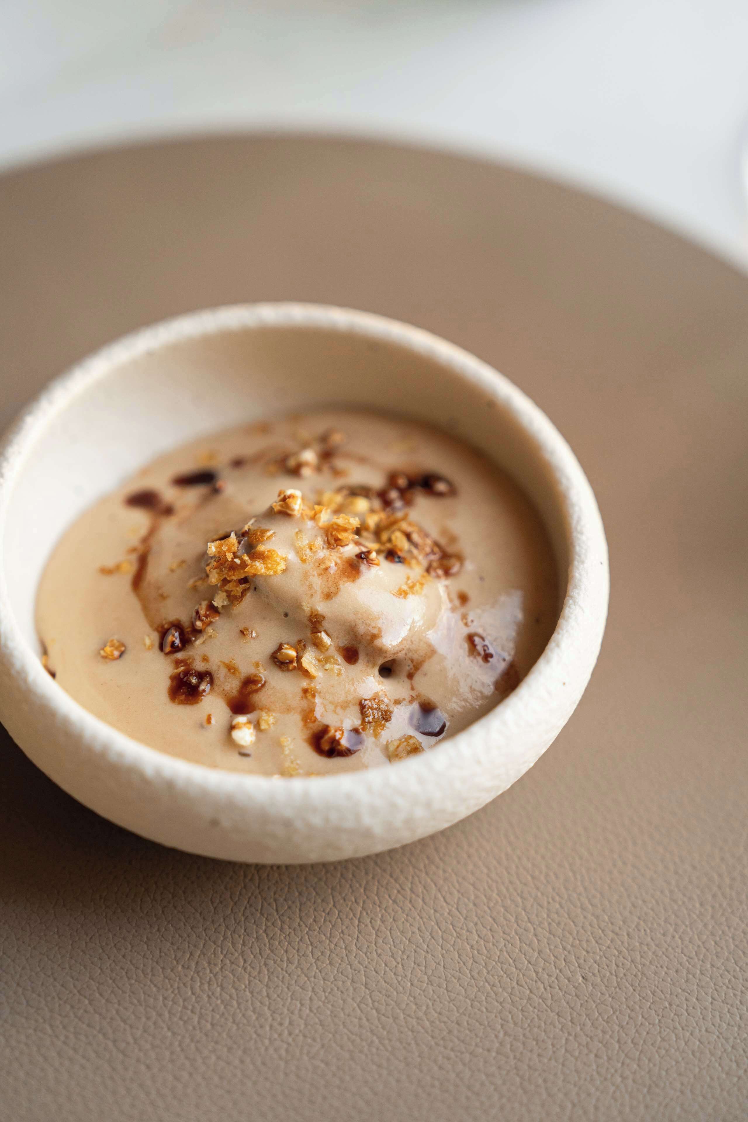A dessert in a ceramic bowl with a caramel drizzle and granola on top.