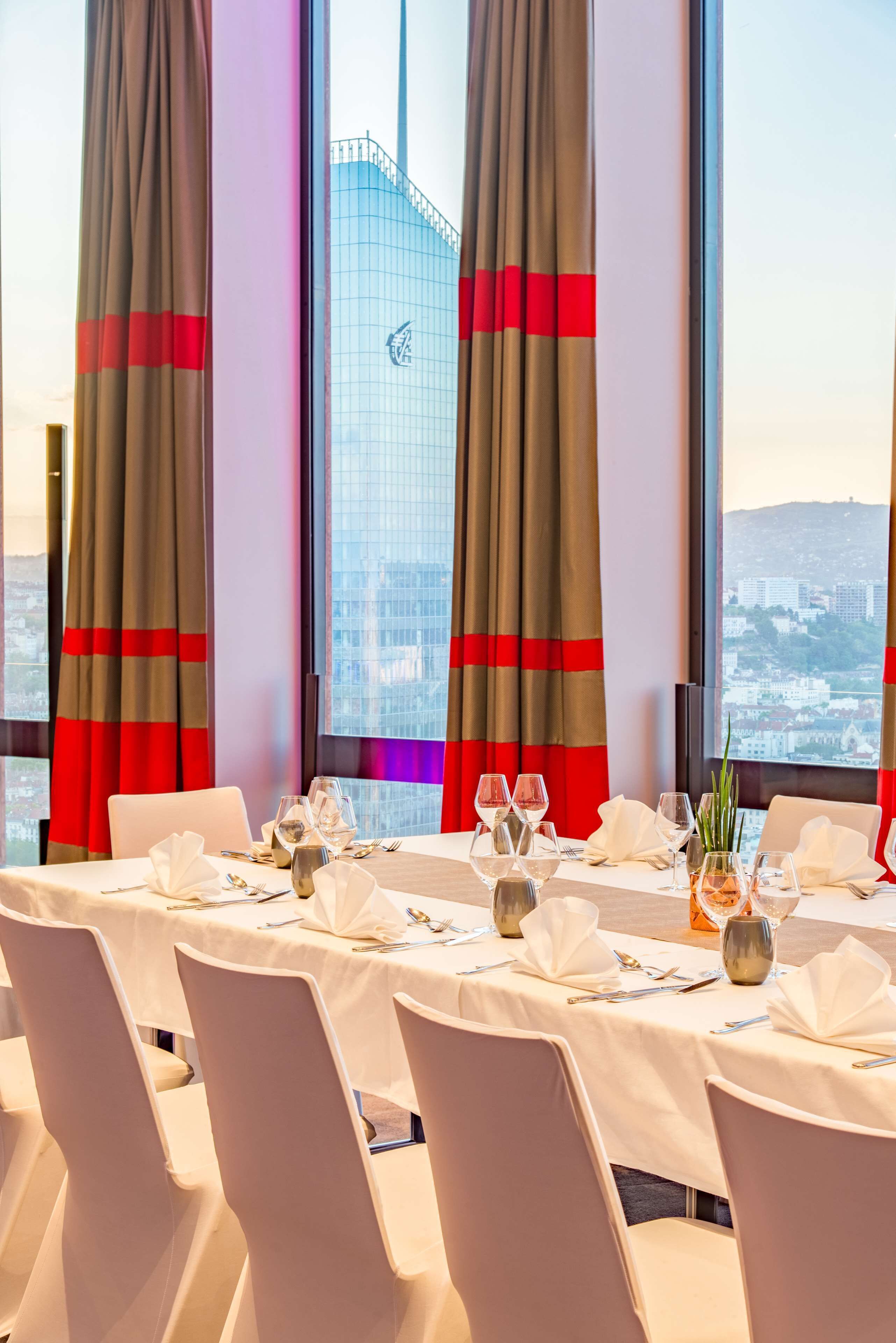 A dining area with a table set for four, large windows with curtains, and a cityscape view.