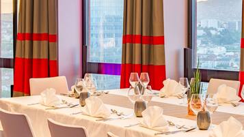 A dining area with a table set for four, large windows with curtains, and a cityscape view.