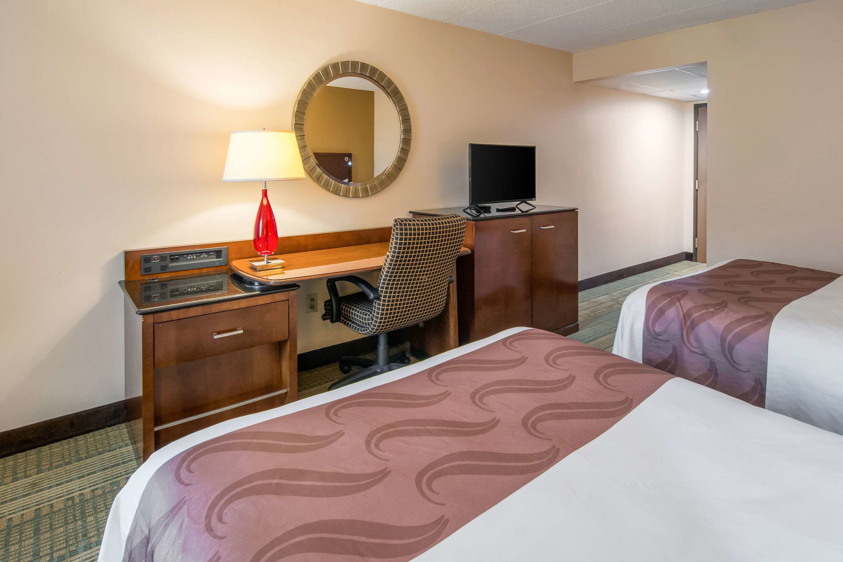 A hotel room with two beds, a desk with a computer, a chair, a TV, and a mirror.