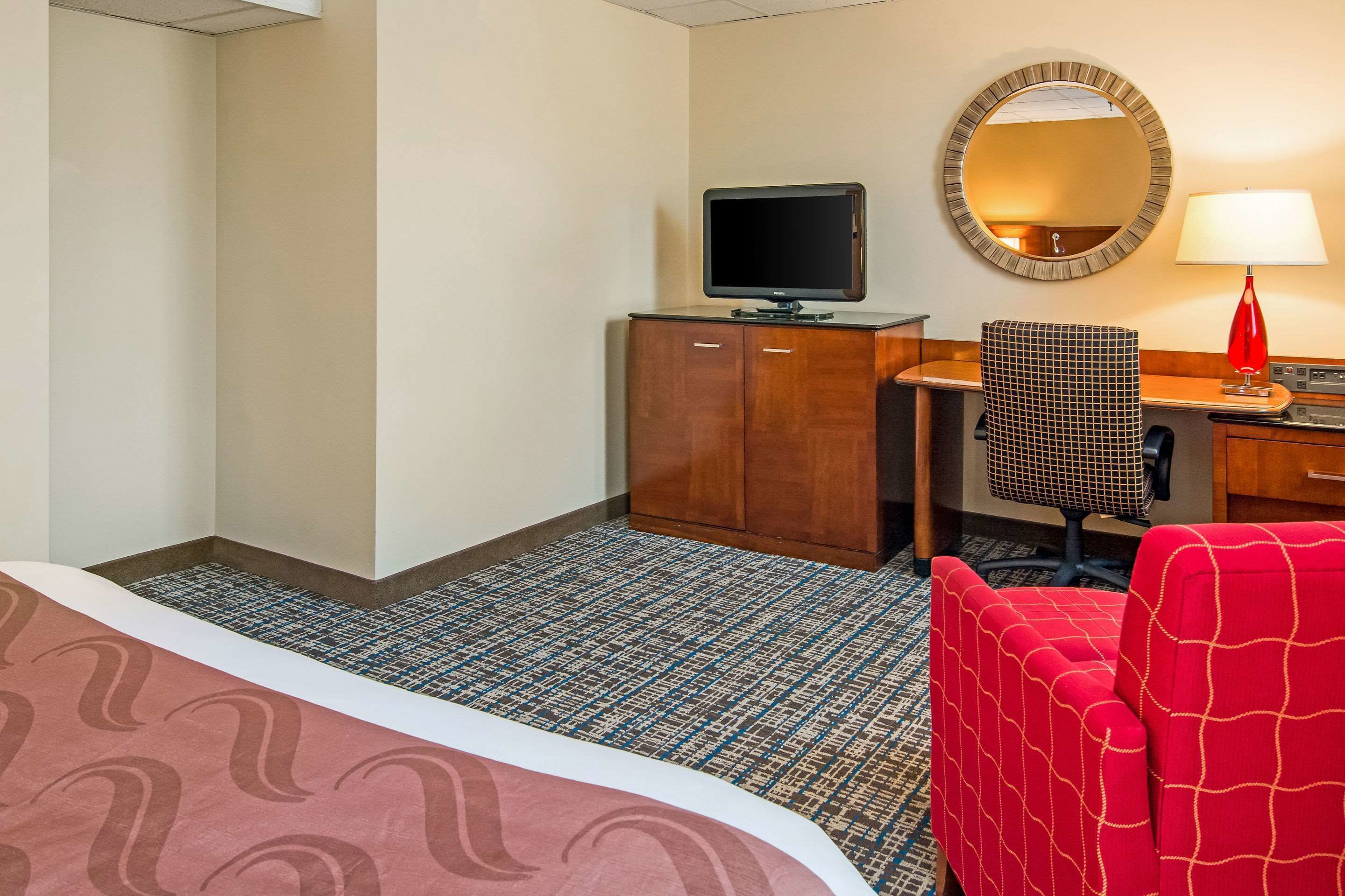 Une chambre d’hôtel équipée d’un lit, d’un bureau avec un ordinateur, d’une chaise, d’une télévision et d’une lampe.
