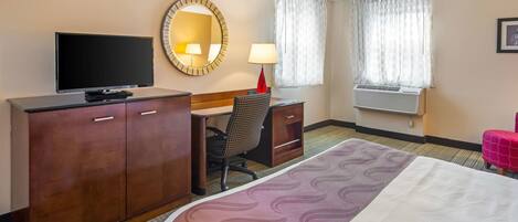 Habitación de hotel con cama, escritorio con silla, televisor, armario, lámpara y ventana con cortinas.