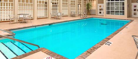 An indoor swimming pool with clear water, surrounded by glass walls and a tiled floor.