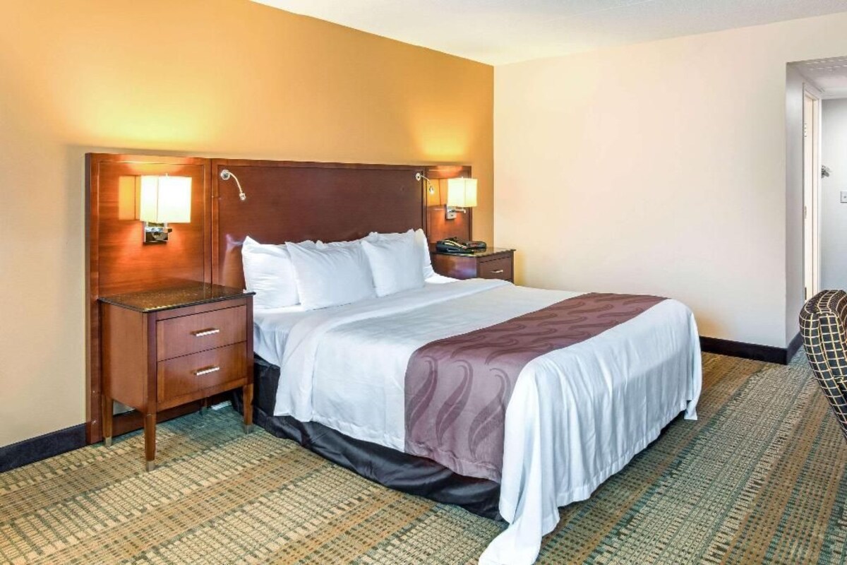 A hotel room with a bed, bedside tables, lamps, and a carpeted floor.