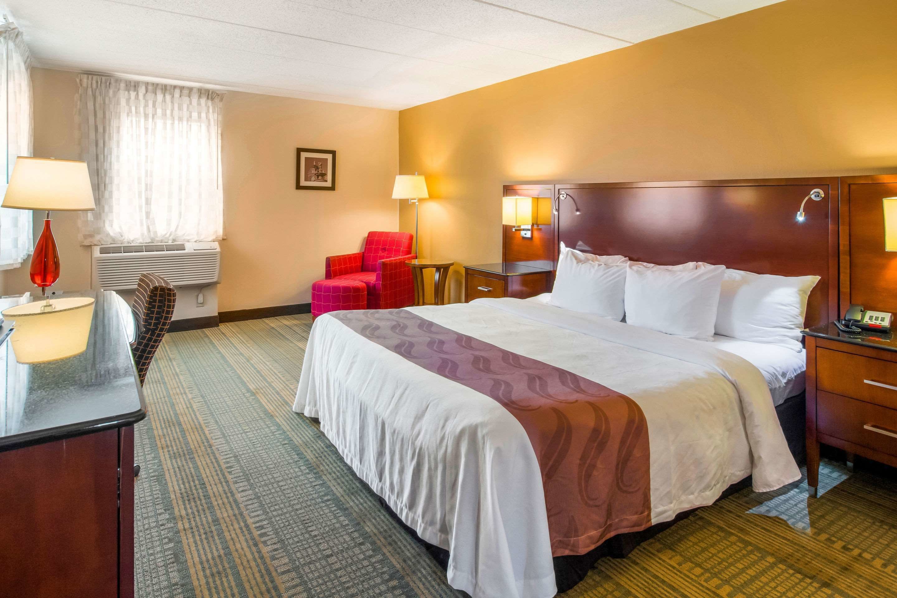 Une chambre d’hôtel avec un grand lit, un bureau avec une lampe, une chaise et une table de chevet avec un téléphone.