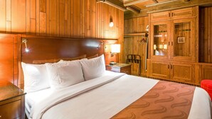 A hotel room with a wooden headboard, a bed with white linens, a nightstand, a desk, and a wardrobe. - Quality Inn & Suites Virginia MN (Virginia)