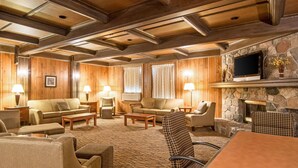 A spacious living room with wooden walls and ceiling, furnished with sofas, armchairs, and a coffee table. A stone fireplace and a flat-screen TV are mounted on the wall. - Quality Inn & Suites Virginia MN (Virginia)