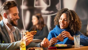 A couple dining at a restaurant with a casual setting, including a table with a drink and a sandwich.