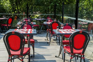 An outdoor dining area with tables and chairs, surrounded by a glass fence, and trees in the background. - ibis Metz Woippy (Woippy)