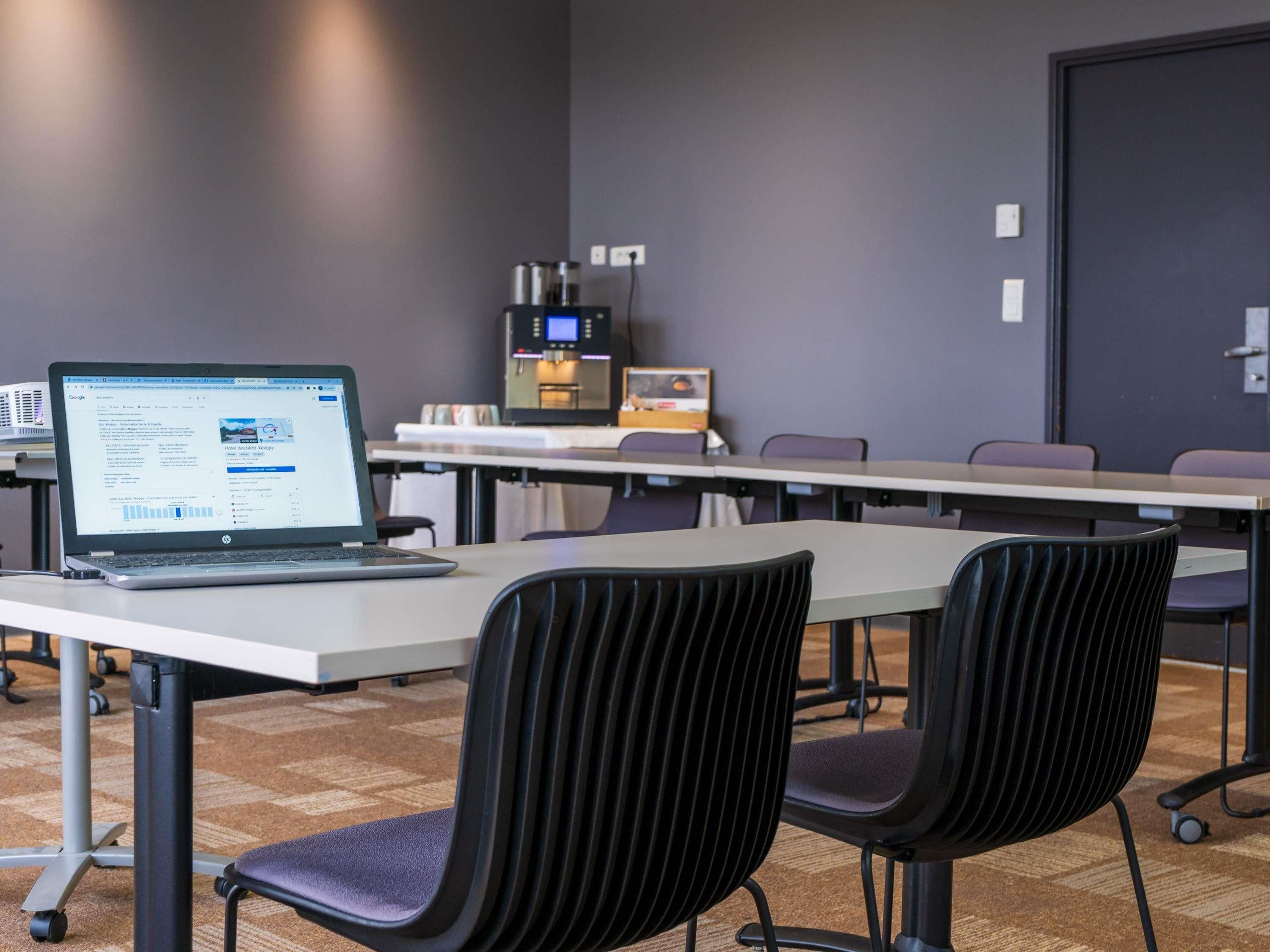 Un salón de conferencias con una laptop sobre una mesa, sillas, una máquina de café y una puerta.