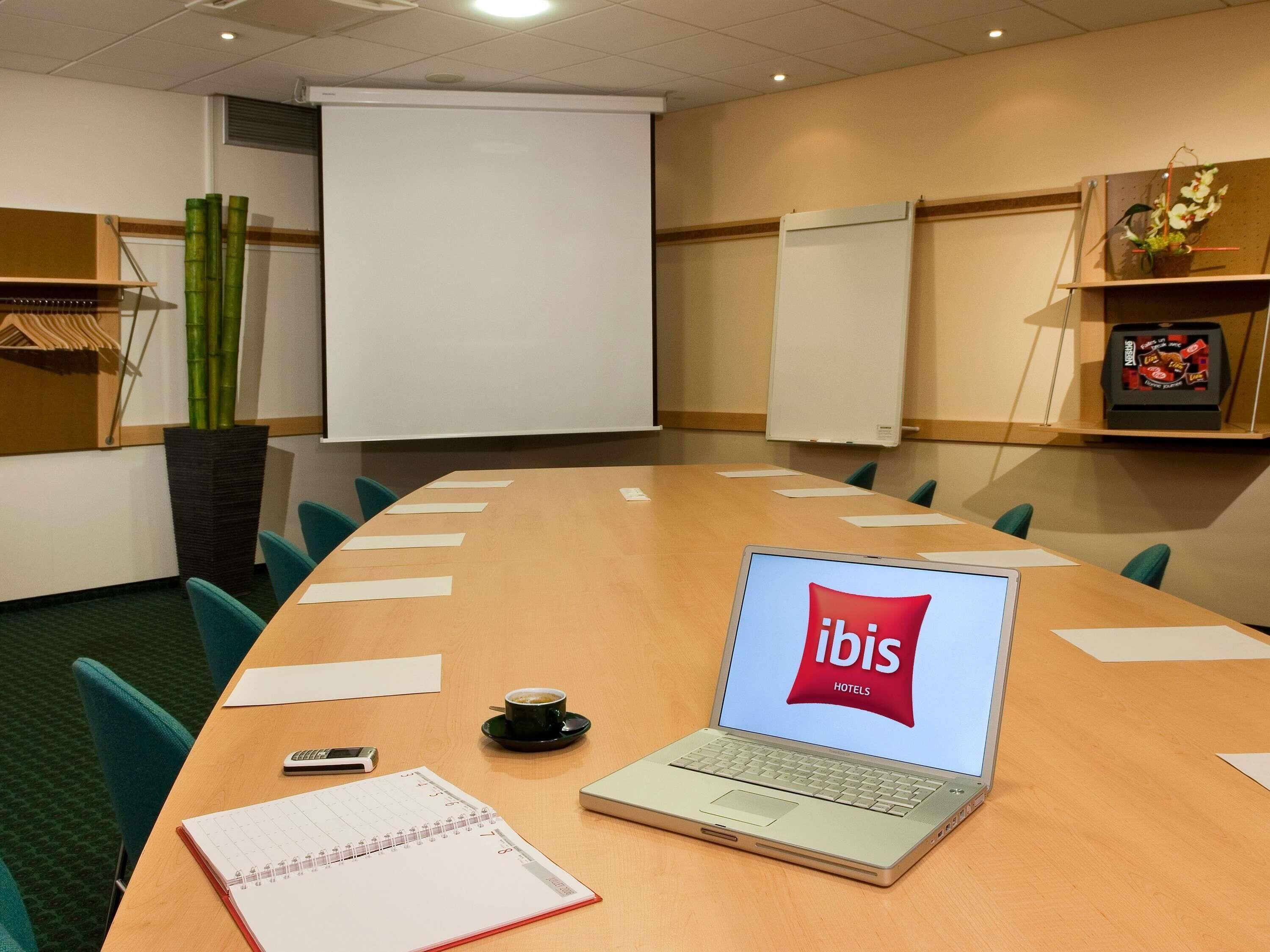 A conference room with a laptop displaying 'ibis Hotels' on the screen, a calendar, a mobile phone, and a coffee cup on the table.