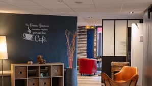 A modern cafe interior with a wall-mounted sign, a wooden console with baskets, a red chair, and a large vase with branches.