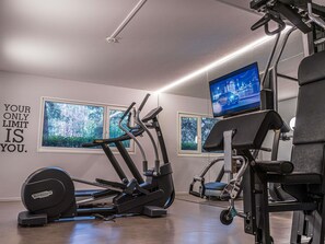 Un gimnasio con equipamiento de ejercicio, una frase motivacional en la pared y un televisor mostrando un automóvil.