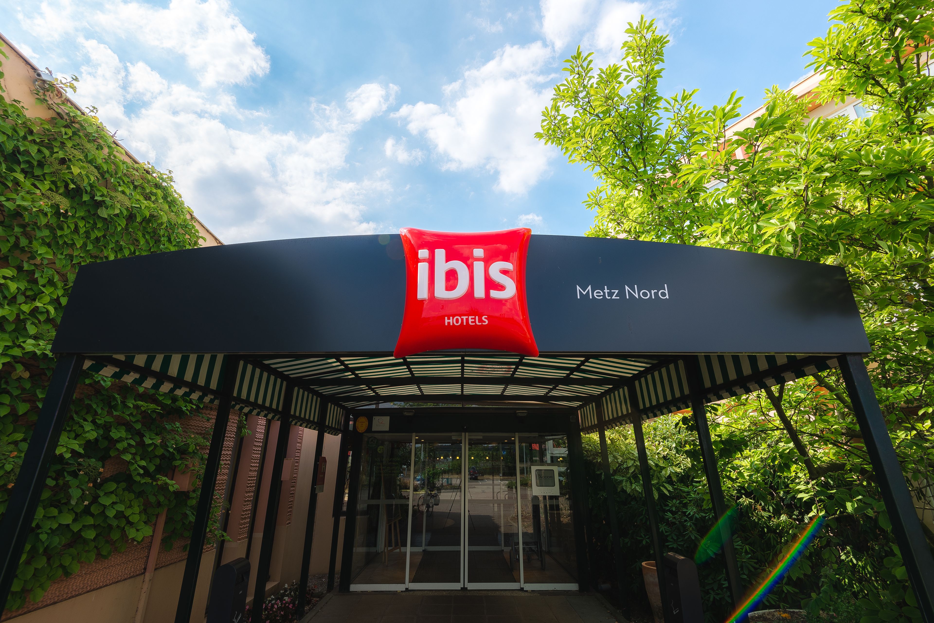 The entrance to a hotel with a glass facade and a red sign indicating it's an ibis hotel.